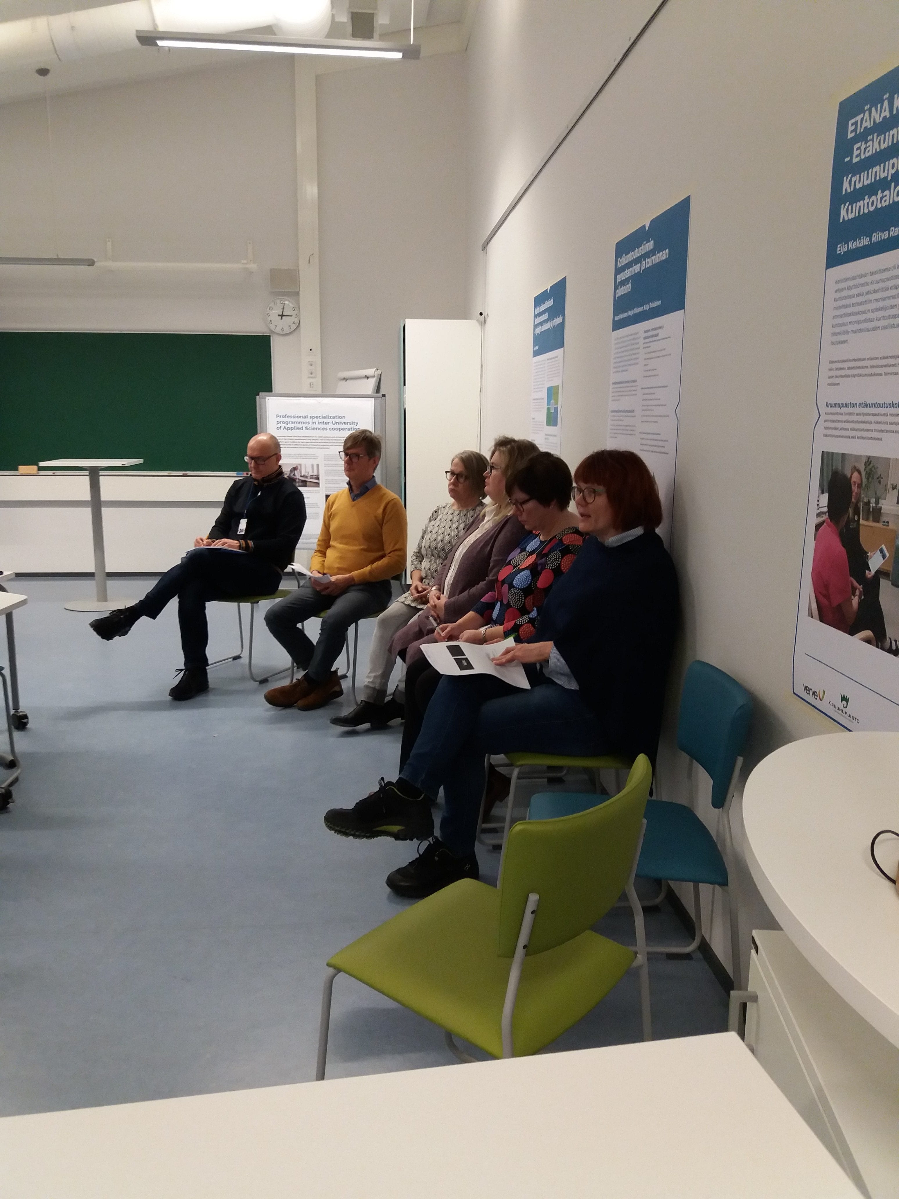 Ihmiset rivissä luokan seinustalla kuuntelemassa seminaariesityksiä.