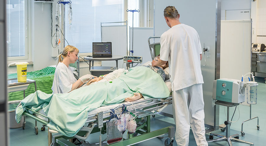 Kaksi opiskelijaa hoitavat sairaalasängyssä makaavaa simulaationukkea.