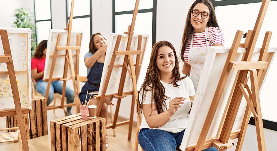 Nuoria naisia studiotiloissa maalamassa tauluja yhdessä.