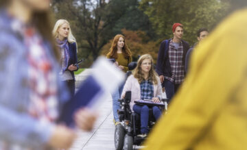 Opiskelijoita kävelemässä ulkona. Yksi opiskelija istuu pyörätuolissa.