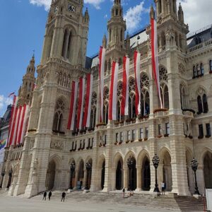 Kuvassa näkyy Wienin kaupungintalo, joka muistuttaa goottilaisia katedraaleja ja rakennuksen etuyläosaan on kiinnitetty punavalkoisia pitkiä viirejä.
